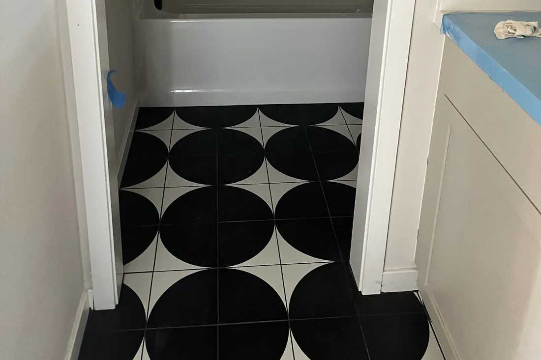 Black and white circle-pattern porcelain tile floor installed in a bathroom with tub and subway tile surround, by My-Key Tile & Flooring