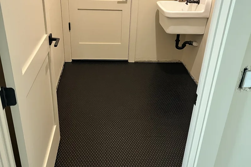 Matte black penny-round mosaic tile floor in a laundry room with wall-hung utility sink, installed by My-Key Tile & Flooring