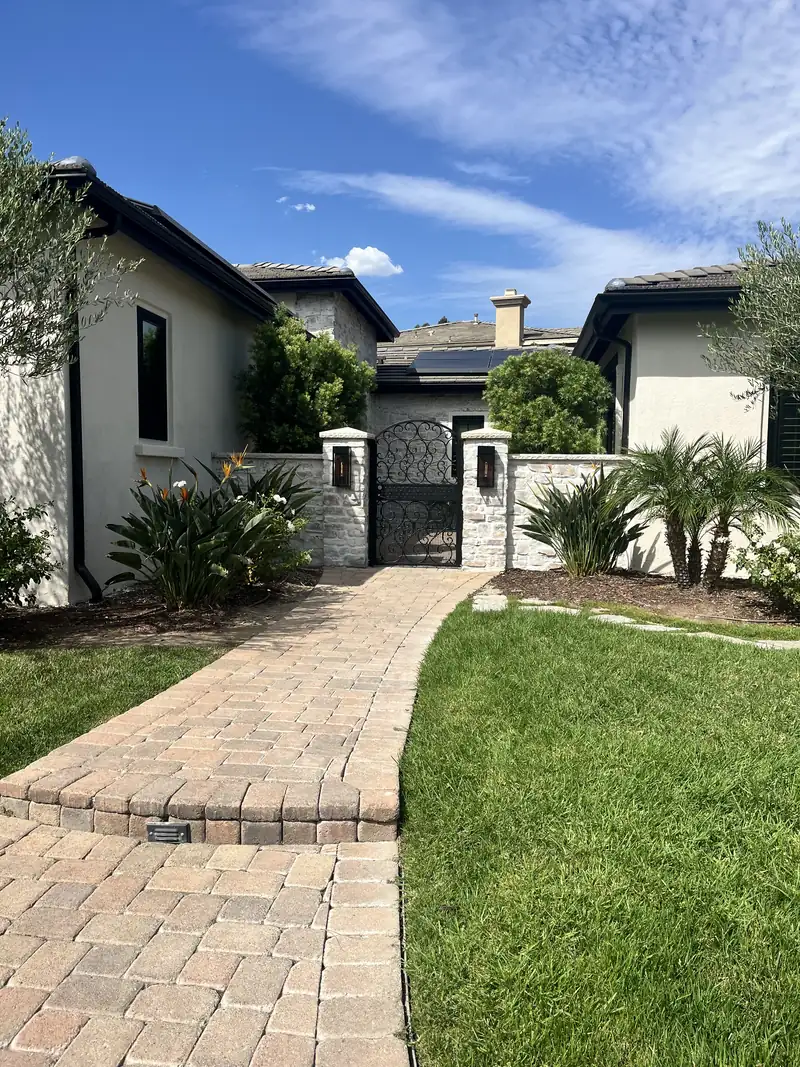 Finished courtyard entrance with a clean paver walkway, stone walls, and iron gate